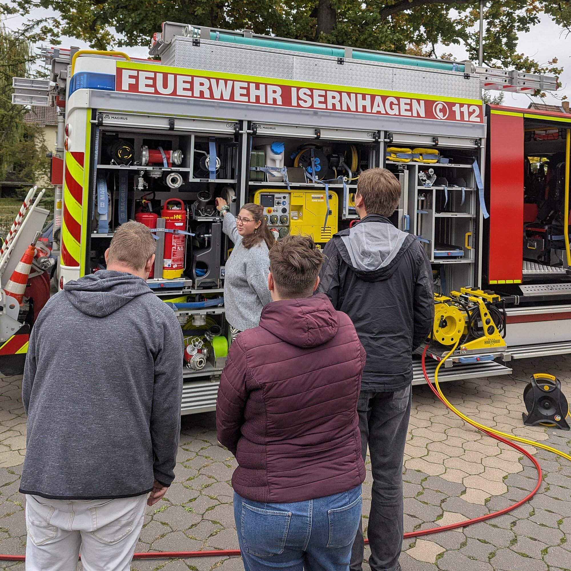 Der Einsatzwagen der Feuerwehr wird erklärt. Vier Personen stehen davor. Eine Person erklärt