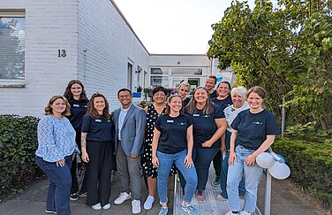 10 Mitarbeiterinnen der Frühförderung stehen vor einem weißen Haus. Mit auf dem Teamfoto sind außerdem die Geschäftsführerin Katharina Külp und der Bereichsleiter Kendrick Macasero zu sehen. 