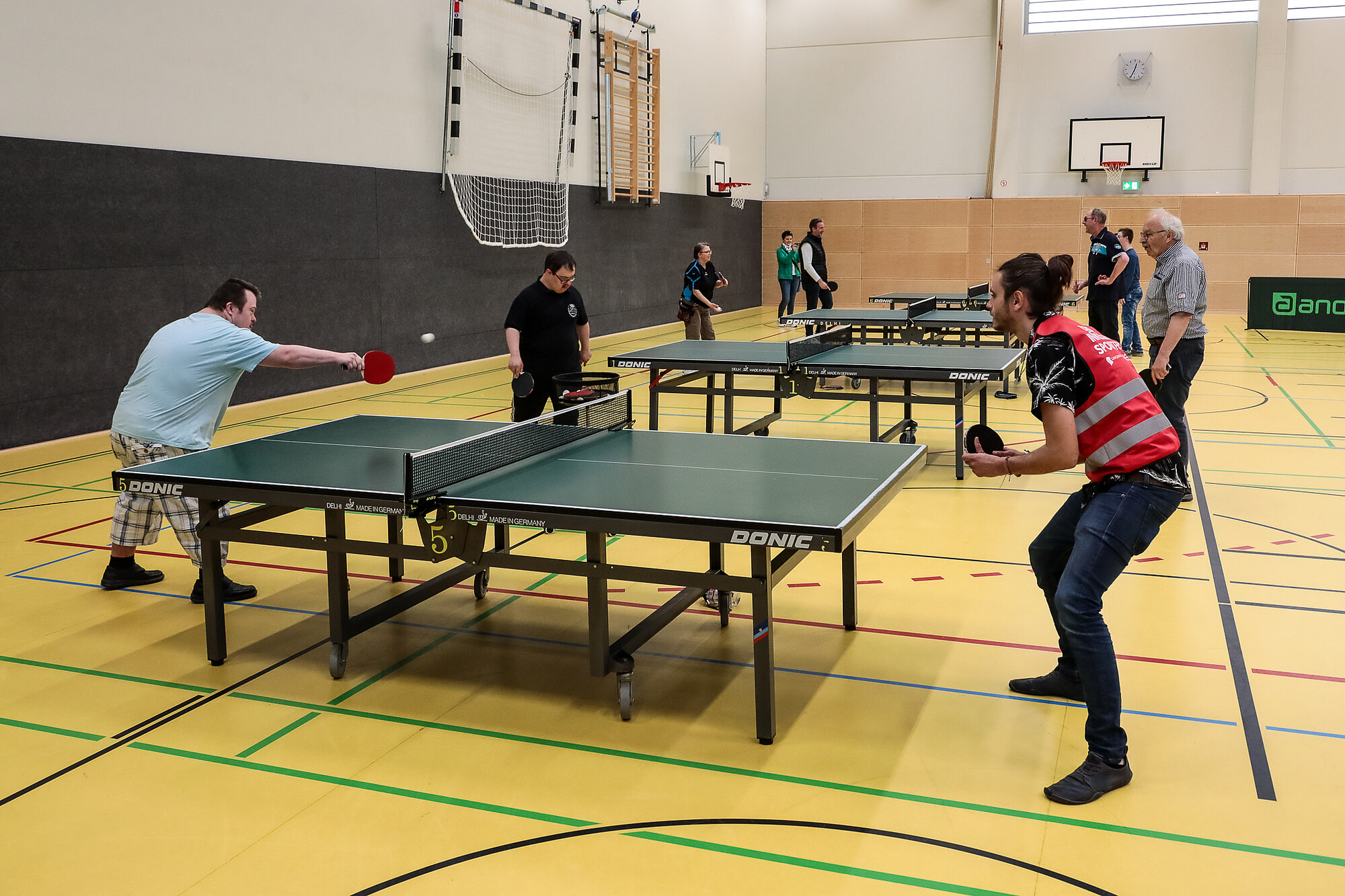 Vier Tischtennisspieler hintereinander und an jeder spielen zwei Menschen Tischtennis gegeneinander