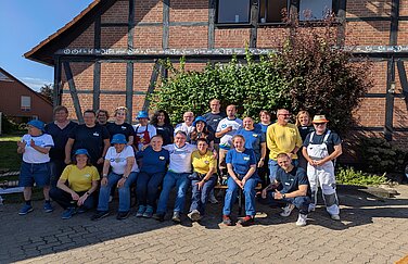 21 Menschen stehen vor einem Fachwerkhaus, dem Lindenhof. Es handelt sich um Ikea Mitarbeitende sowie Mitarbeitender und Klient*innen der Lebenshilfe Langenhagen-Wedemark.