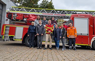 Gruppe von Menschen stehen vor einem Feuerwehrauto mit Drehleiter 