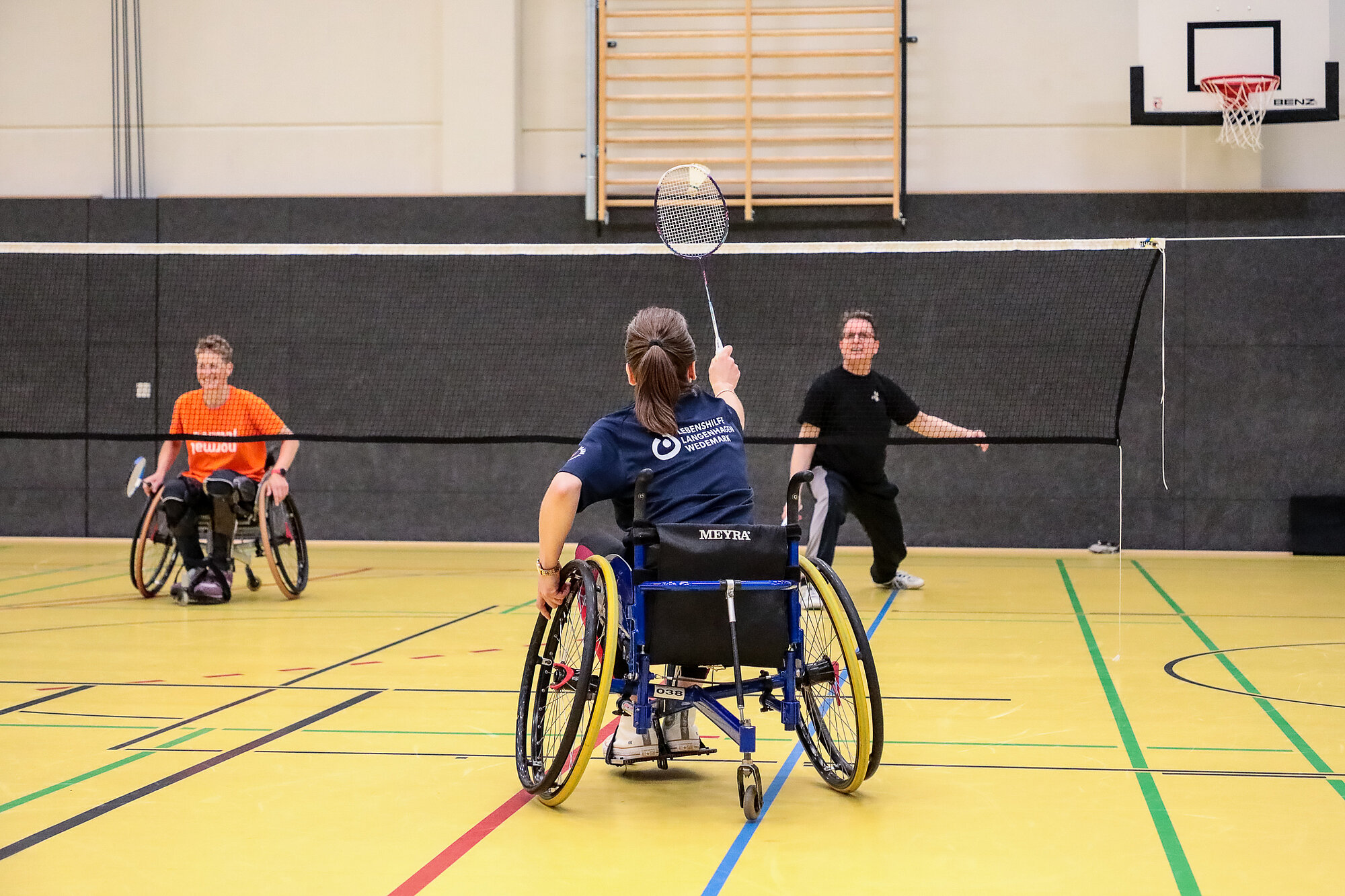 zwei Menschen im Rollstuhl und einer ohne spielen Badminton
